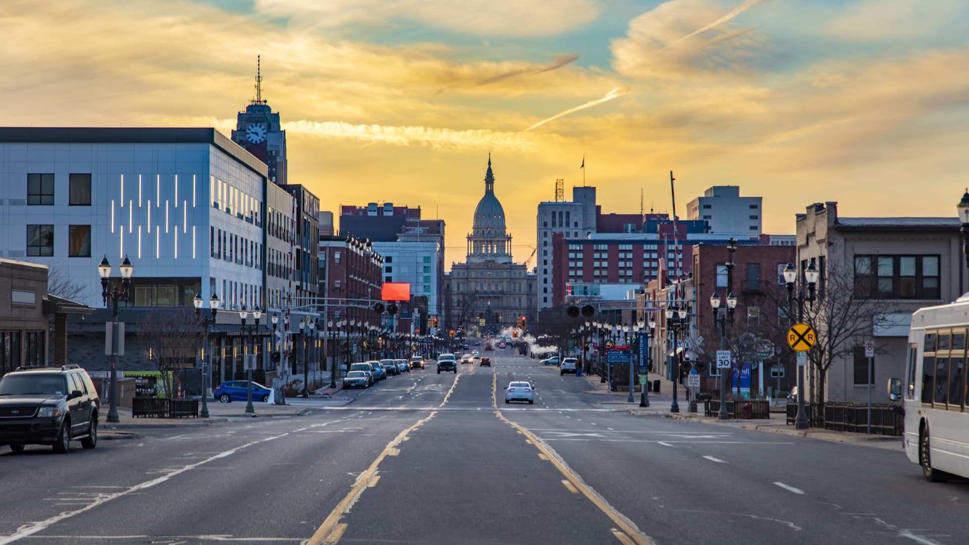 A picture taken of Downtown Lansing, at street level, showcasing many shops, building and bustling morning activity.